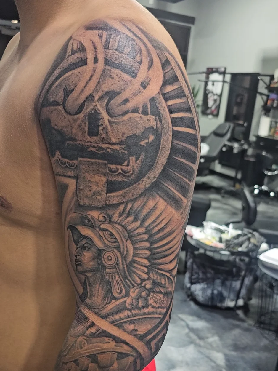Aztec skull with warrior headdress tattoo on upper arm by Alex Zamora